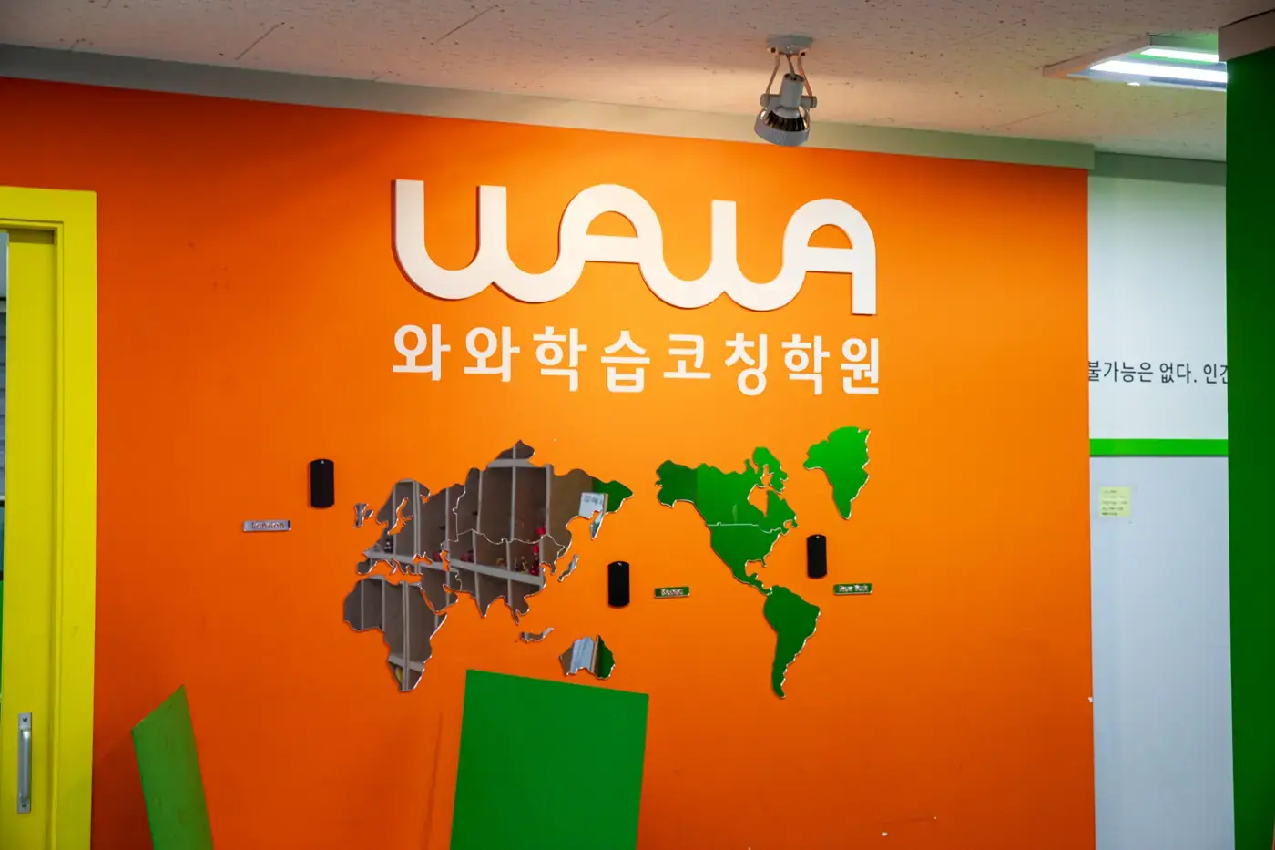 주황색 벽에 흰 와와학습코칭학원 로고와 세계지도 장식이 붙은 철산점 입구 공간